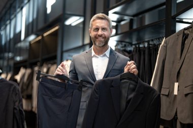 Bir adam butikte alışveriş yaparken klasik bir terzi kıyafeti giyer. Başarılı bir iş adamı için klasik bir kıyafet. Takım elbiseli modaya uygun bir mağaza. İş adamı takım elbise seçer. Bir erkek resmi etkinlik için takım elbise seçer.