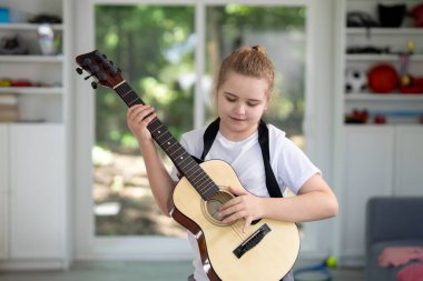 Akustik gitar çalan komik çocuk. Çocuk oturma odasında gitar çalışıyor. Genç gitarist içeride müzik öğreniyor. Müzik dersi sırasında gitar çalan bir çocuk. Çocuk odada gitar çalıyor.
