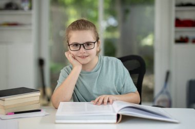 Evde kitap okuyan sevimli bir çocuk. Akıllı çocuk ders kitaplarıyla çalışıyor. Öğrenci, rahat bir odada kitap ödevi okuyor. Öğrenci çocuk kitap okumaya odaklandı. Sınıfta masal okuyan zeki çocuk.