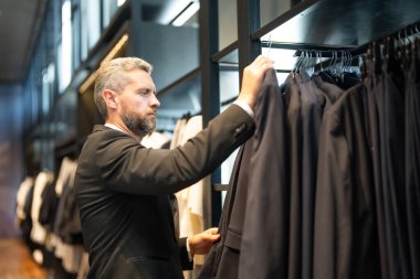 Bir adam butikte alışveriş yaparken klasik bir terzi kıyafeti giyer. Başarılı bir iş adamı için klasik bir kıyafet. Takım elbiseli modaya uygun bir mağaza. İş adamı takım elbise seçer. Bir erkek resmi etkinlik için takım elbise seçer.