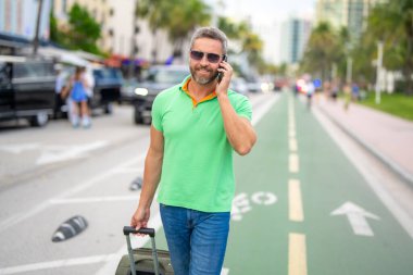 Dışarıda telefonu olan olgun bir gezgin. Bahar tatilindeki turist gezgini. Bahar gezisi için seyahat valizleri. Yaz turu. Tropik bir kaçamak. Bahar tatili. Bir gezgin yaz gününün tadını çıkarır. Yaz gezisi