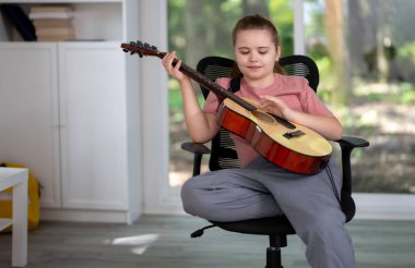 Gitar çalan çocuk. Çocuk oturma odasında gitar çalma alıştırması yapıyor. Çocuk içeride gitar öğreniyor. Müzik dersi sırasında gitarlı bir çocuk. Akustik gitar çalan bir çocuk. Çocuk şarkıları çalışıyor