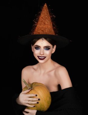 Halloween girl with makeup and witch hat. Halloween witch posing with pumpkin. Halloween party banner. Woman portrait with pumpkin. Halloween witch character. Sexy boo model in witch costume