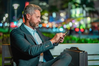 Dışarıda tablet üzerinde çalışan bir iş adamı. Tabletli bir iş adamı. Gece sokağında tabletli bir iş adamı. Tablet kullanan bir işadamı, bankta oturur. Gece işi.