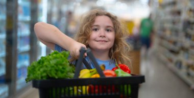 Süpermarkette alışveriş arabası olan bir çocuk. Çocuk taze sebze seçiyor. Yakışıklı çocuk sağlıklı yiyecek için alışveriş yapıyor. Süpermarketteki çocuk. Süpermarketteki çocuk. Çocuk süpermarketten sebze alıyor.