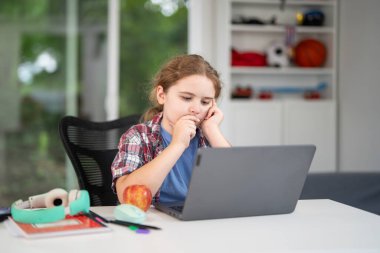 Evde dizüstü bilgisayar ve kitaplarla çocuk eğitimi. Rahat bir sınıfta çocuk öğreniyor. Sınıfta çocuk eğitimi. Çevrimiçi öğrenme. Çocuk düşünme konsepti. Evde çocuk eğitimi. Okullu çocuk evde.