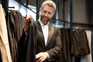 Bir butik danışmanı müşterinin mükemmel takımı bulmasına yardım eder. Lüks bir giysi koleksiyonu. Zarif takım iş adamı için mükemmel. İyi dikilmiş bir takım.