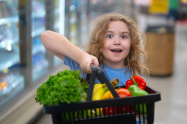 Marketteki çocuk. Çocuk markette meyve seçiyor. Çocuklar için market eğlencesi. Çocuk markette taze meyve topluyor. Markette elinde sebze sepeti olan genç bir müşteri. Çocuk marketten alışveriş yapıyor.