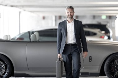 Takım elbiseli yakışıklı bir iş adamı. Lüks bir arabanın yanında zengin bir işadamı. Küresel. Başarılı bir iş. Pahalı arabanın önünde zarif bir iş adamı. Başarılı iş adamı