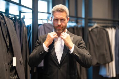 İş adamı için uygun. İyi giyimli bir erkek model bir butikte poz veriyor. Perakende satış elemanı şık bir adamın mükemmel takımı bulmasına yardım eder. Bir mağaza müdürü şık bir takım elbise ayarlar.