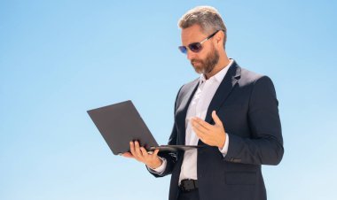 İş adamı dışarıda dizüstü bilgisayar kullanıyor. Dizüstü bilgisayarı olan olgun bir iş adamı. Dizüstü bilgisayarı olan ciddi bir iş adamı. İnternette iş. İş adamı laptoptaki verileri kontrol ediyor. Takım elbiseli iş adamı internette çalışıyor.