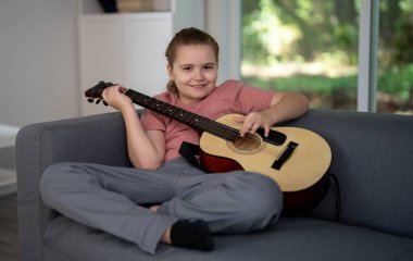 Gitar çalan çocuk. Çocuk oturma odasında gitar çalma alıştırması yapıyor. Çocuk içeride gitar öğreniyor. Müzik dersi sırasında gitarlı bir çocuk. Akustik gitar çalan bir çocuk. Çocuk şarkıları çalışıyor