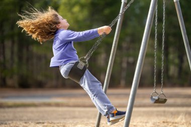 Bahar parkında sallanan neşeli çocuk. Sarı saçlı küçük bir çocuk salıncakta sallanıyor. Parkta gülümseyen mutlu çocuk. Mutlu çocukluk anları. Çocuk dışarıda oynuyor. Çocuk salıncakta eğleniyor. Çocuklar için açık hava oyunu