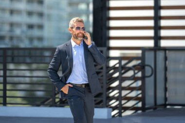 İş adamı yürüyor ve telefonla arıyor. Kendine güvenen bir iş adamının önemli bir çağrısı var. İş görüşmesi. Telefon görüşmesi. Patron telefonla konuşmakla meşgul. Zengin iş adamı. İş çağrısı