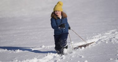 Çocuklar kış oyunu oynuyor. Komik çocuk karda kış şapkasıyla oynuyor. Sıcak giysili mutlu çocuk kar yağarken eğleniyor. İlk kar yağışında çocuk dışarıda karla oynuyor. Çocuklar için kış aktiviteleri