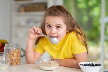 Child eating healthy breakfast at home kitchen. Child at the kitchen dining table. Happy kid having tasty lunch in the modern kitchen. Child during family meal. Teen child eat dinner in white kitchen