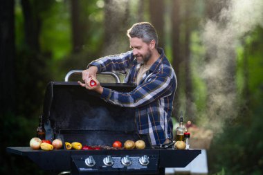 Hafta sonu barbeküde ızgara yapan bir adam. Orta yaşlı erkek şef terasta gurme et pişiriyor. Milenyum adamı akşam yemeği için ızgara yemek yapıyor..