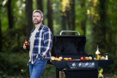 Bahçe barbeküsünde ızgara yapan olgun Latin bir adam. Orta yaşlı erkek şef ızgara terasında gurme eti pişiriyor. Açık hava ızgarası. Bahçe ızgarasında ızgara et.