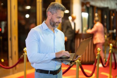 Gece sokakta dizüstü bilgisayar kullanan bir iş adamı. İş adamı dışarıda dizüstü bilgisayarda çalışmayı planlıyor. İşadamı, neon şehir ışıkları altında dizüstü bilgisayarda geziniyor. Serbest çalışan bir iş adamı. Gece işi.