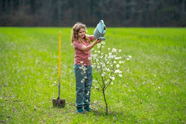 Çocuk dışarıya bir bahar ağacı dikiyor. Çocuklar meyve ağacı gibi büyür. Kürekli çocuk bahçıvan. Çocuk meyve bahçesinde çiçek açan ağaçlarla çalışıyor. Çocuklar arka bahçeye ağaç dikiyorlar. Ağaçlarla ilgilenen genç çiftçi