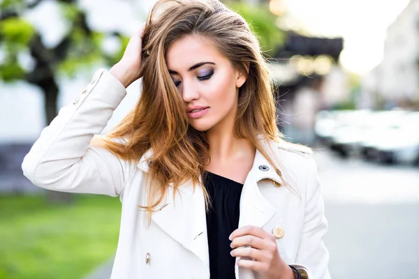 young woman in white trench coat posing on urban background in city