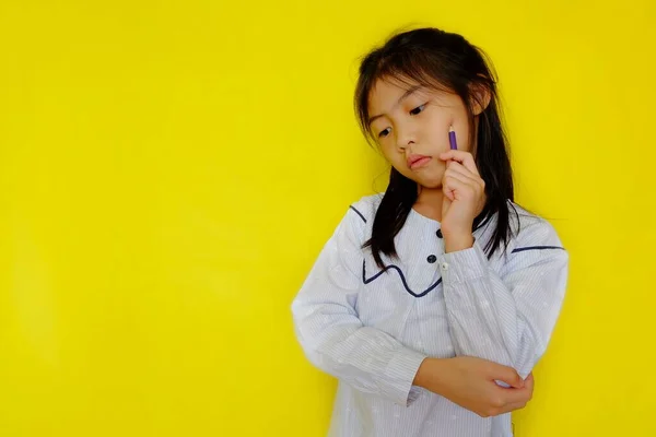 Düşüncelere dalmış, eli yanağında, aşağıya bakıp bir karar vermeye çalışan genç bir Asyalı kız. Parlak sarı arkaplan.