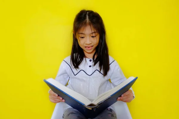 Elinde hikaye kitabı tutan, okuyup eğlenen genç, tatlı bir Asyalı kız. Parlak sarı arkaplan.