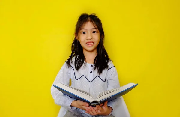 Elinde hikaye kitabı tutan, okuyup eğlenen genç, tatlı bir Asyalı kız. Parlak sarı arkaplan.