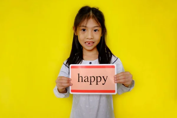 Sevimli genç Asyalı bir kız kendini neşeli, gülümseyen, elinde & quot; Happy & quot; yazan bir tabela tutan. Parlak sarı arkaplan.