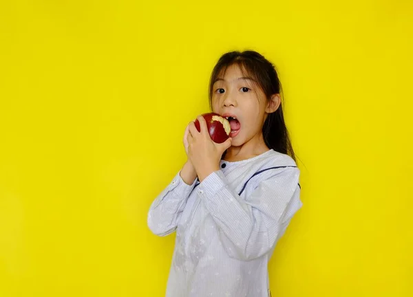 Kırmızı bir elmayı kapıp ondan ısırmaya çalışan genç, tatlı bir Asyalı kız. Parlak sarı arkaplan.