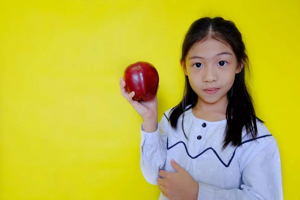 Elinde elma tutan, kahvaltıda yemek için hazırlanan genç, tatlı bir Asyalı kız. Parlak sarı arkaplan.