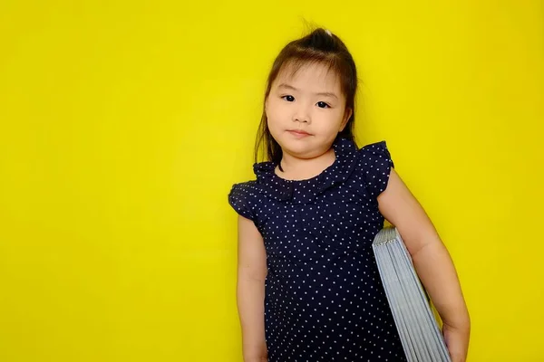 一个可爱的年轻亚洲女孩抱着一本硕大的教科书 面带微笑 准备在学校讲故事 亮黄色背景 — 图库照片