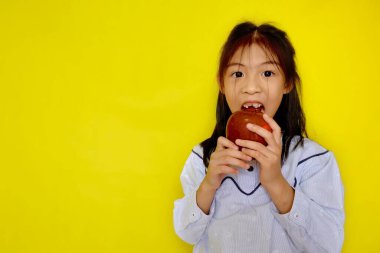 Kırmızı bir elmayı kapıp ondan ısırmaya çalışan genç, tatlı bir Asyalı kız. Parlak sarı arkaplan.