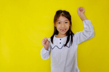 Şirin, zeki, Asyalı bir kız sınıfta bir soruya cevap vermek için heyecanla elini kaldırıyor. Parlak sarı arkaplan.