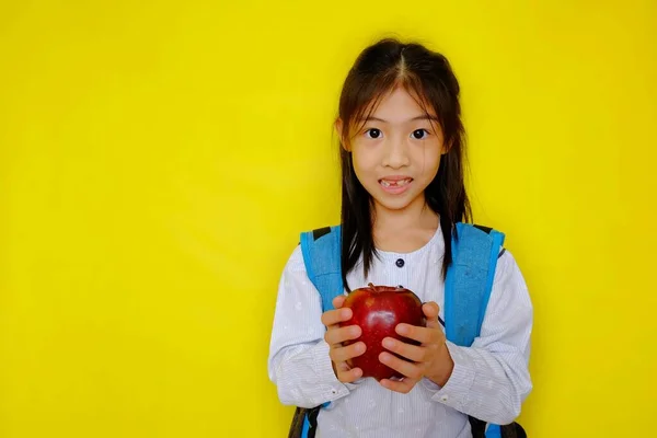 Elinde elma tutan, kahvaltıda yemek için hazırlanan genç, tatlı bir Asyalı kız. Parlak sarı arkaplan.