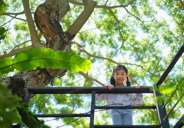 Güzel bir Asyalı kızın, arka planda ağaçlar olan bir güvertenin korkuluğunu tutarken gülümsediği düşük açılı bir kare..