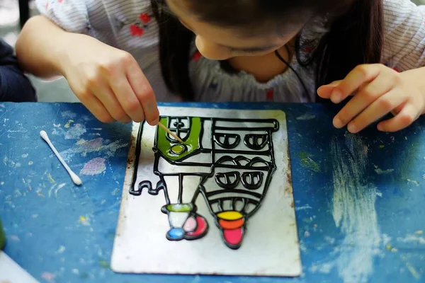 Şirin bir Asyalı kız kreş projesinde çalışıyor. Renkli akrilik boyalarla bir kale çiziyor..