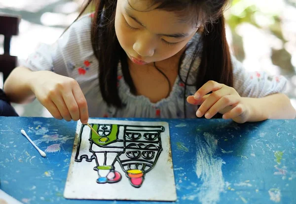Şirin bir Asyalı kız kreş projesinde çalışıyor. Renkli akrilik boyalarla bir kale çiziyor..