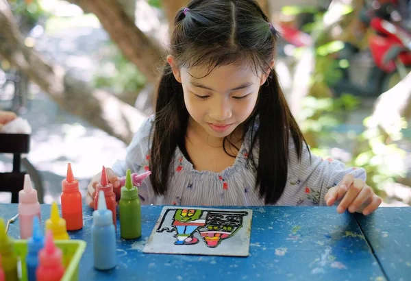 Şirin bir Asyalı kız kreş projesinde çalışıyor. Renkli akrilik boyalarla bir kale çiziyor..