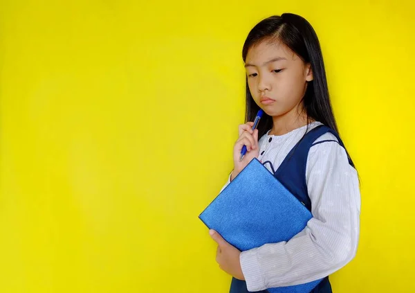 Beyaz ve mavi okul üniforması içinde elinde mavi bir kitapla, okuyup, odaklanarak zor bir sorunu çözmeye çalışan, ciddi görünen genç bir Asyalı kız. Parlak sarı arkaplan.