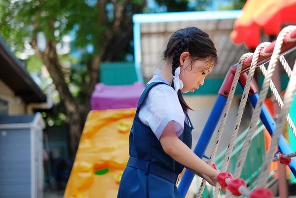 Beyaz ve mavi üniformalı genç bir Asyalı kız tırmanırken tırmanırken spor yapıyor ve eğleniyor..