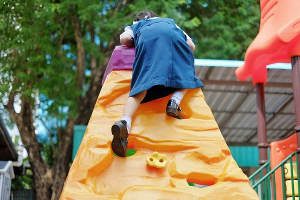 Beyaz ve mavi okul üniformalı yakışıklı bir Asyalı kız çocuk parkında kaya tırmanışı yapıyor, egzersiz yapıyor ve eğleniyor..