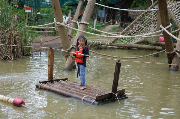 一个身穿橙色救生衣的可爱的年轻亚洲女孩 正在用竹筏穿过一条小运河 用绳子拉着自己 玩得很开心 但很安全 图库图片