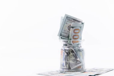100 dolarlık banknotlarla dolu bir kavanoz dolusu para üzerine oturmuş. Beyaz negatif boşluk, kopyala uzayı. Muhasebe, emeklilik, eğitim için tasarruf kavramı.