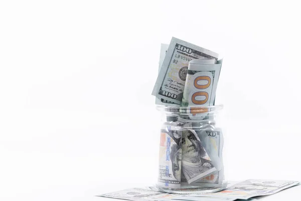 100 dolarlık banknotlarla dolu bir kavanoz dolusu para üzerine oturmuş. Beyaz negatif boşluk, kopyala uzayı. Muhasebe, emeklilik, eğitim için tasarruf kavramı.