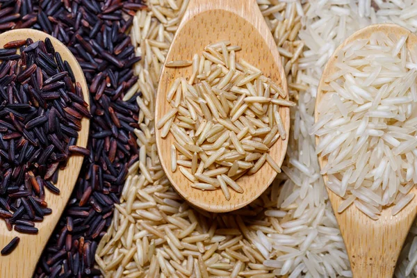 Black wild rice, brown wild rice and white jasmine rice in wooden spoon flat lay. Creative layout. Food concept