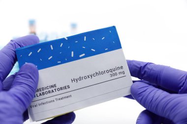 Dubai-UAE-Circa 2020: Doktor covid-19 tedavisi için bir kutu ilaç gösterdi. Arka planda kan testleri tüpleri bulunan hidroklorokin ilaç kavramı. Coronavirüs için tedavi, COVID-19.