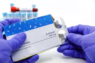 Dubai-BAE-Circa 2020: Doktor covid-19 tedavisi için bir kutu ilaç gösterdi. Arka planda kan testleri tüpleri bulunan Avifavir ilacı kavramı. Coronavirüs için tedavi, COVID-19.