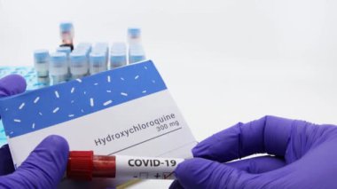 Dubai-UAE-Circa 2020: Doktor covid-19 tedavisi için bir şişe ilaç gösteriyor. Arka planda kan testleri tüpleri bulunan hidroklorokin ilaç kavramı. Coronavirüs için tedavi, COVID-19.