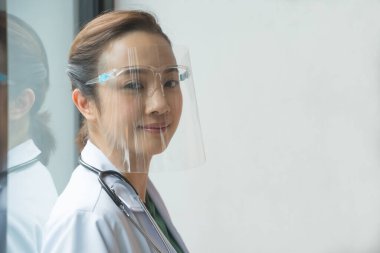 Asyalı kadın doktorlar, Gene 'in hastanedeki pencerenin yanında olduğu virüslerden korunmak için yüz koruyucu takıyorlar. Hastane personeli kavramı.